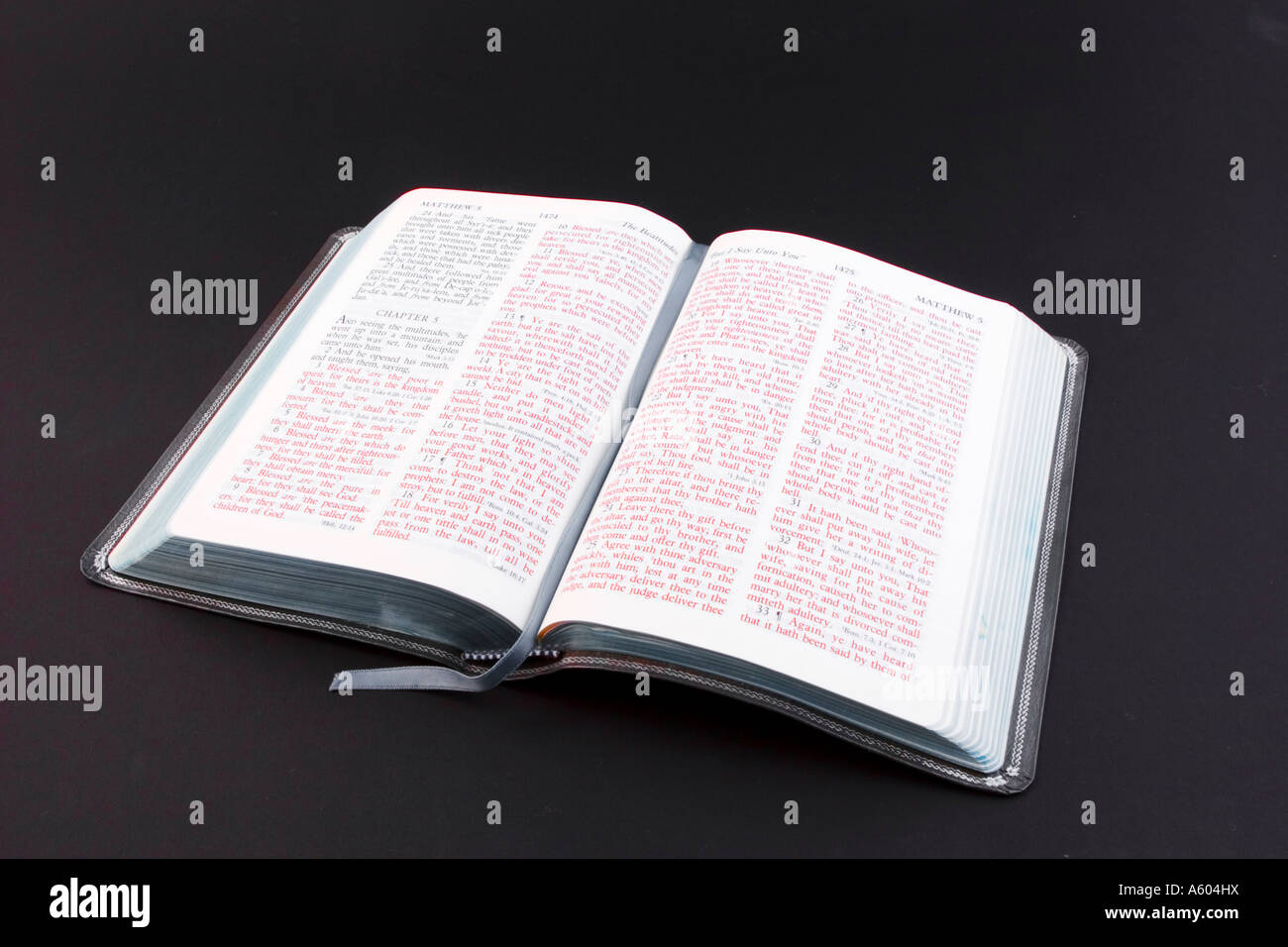 Open Holy Bible with pages showing both black and red lettered text on black horizontal background Stock Photo