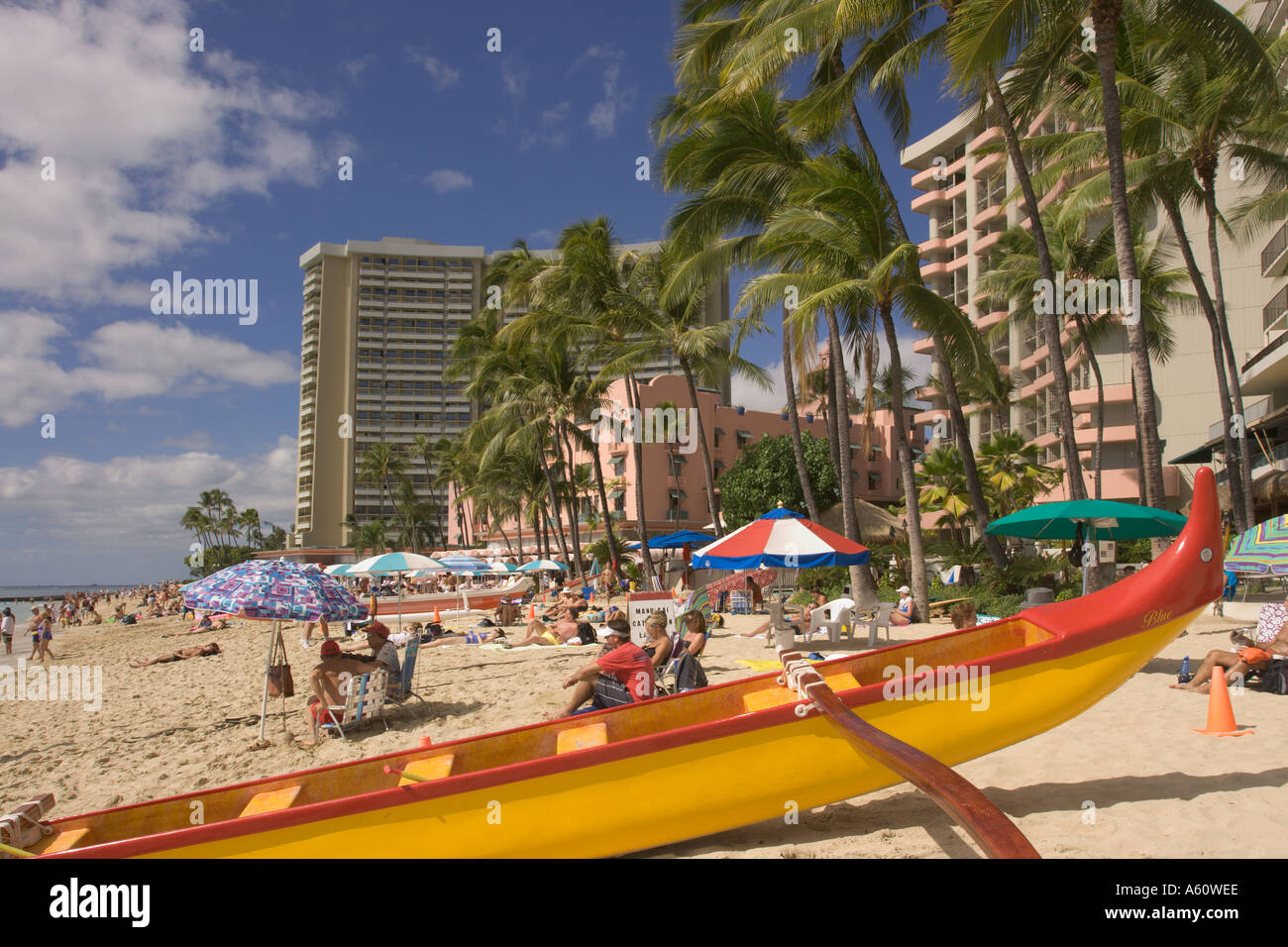 View along Waikiki Beach red & yellow outrigger canoe pulled up on beach blue sky with white