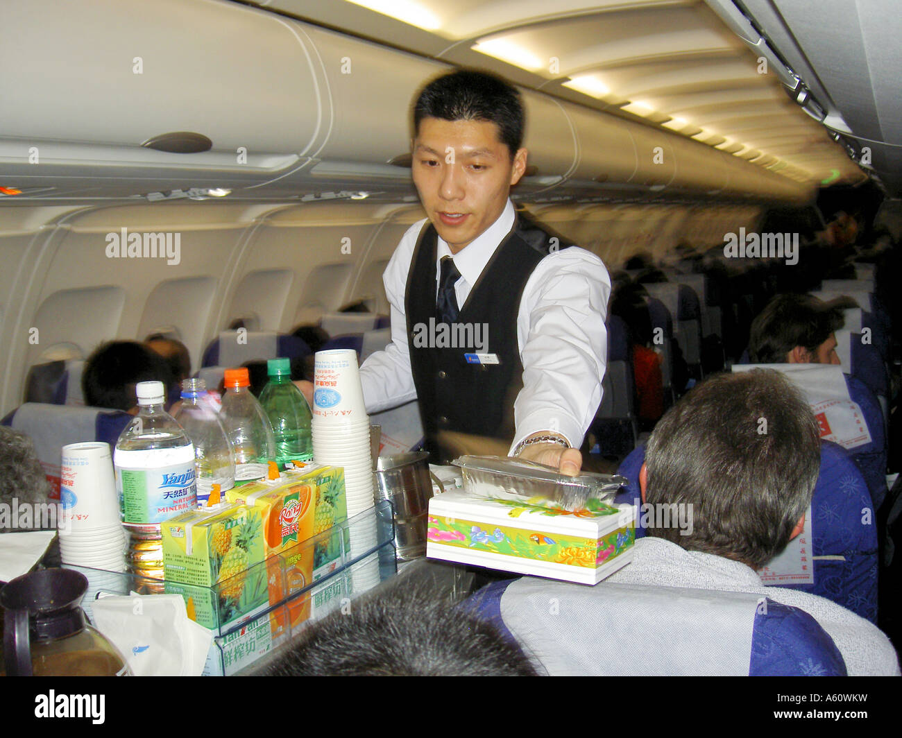 Flight attendant on Hainan Airlines flight aircraft serving meal package lunch dinner to passenger from aisle trolley, China Stock Photo