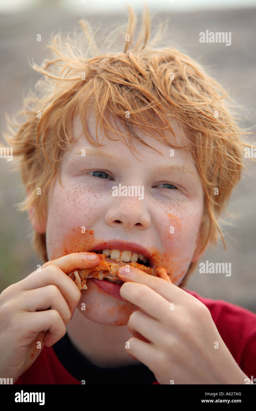 portrait of a young red haired boy with freckles eating a chicken wing Stock Photo