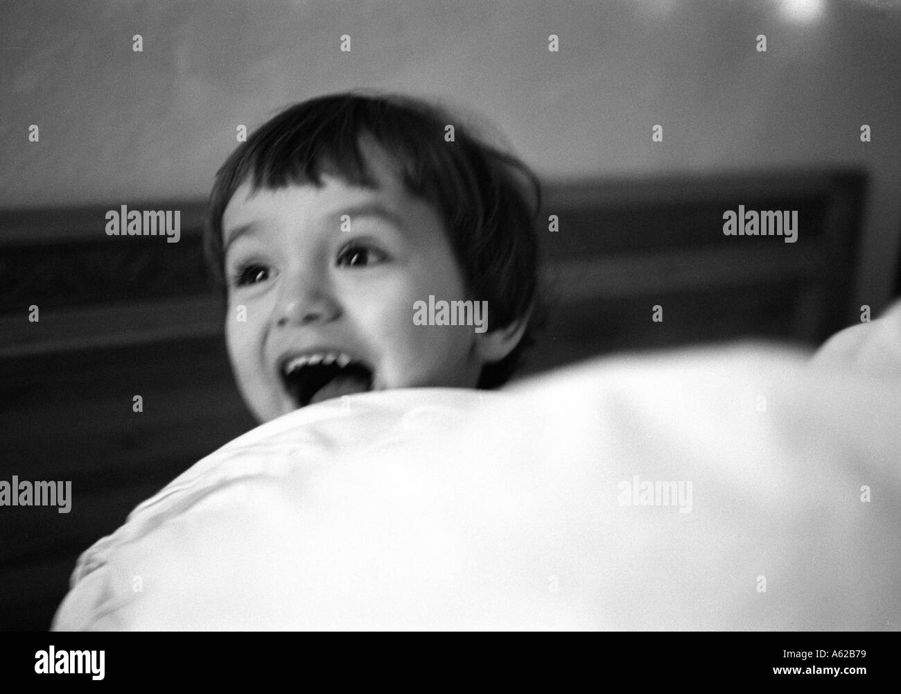 young boys head poking out from behind duvet laughing and shouting