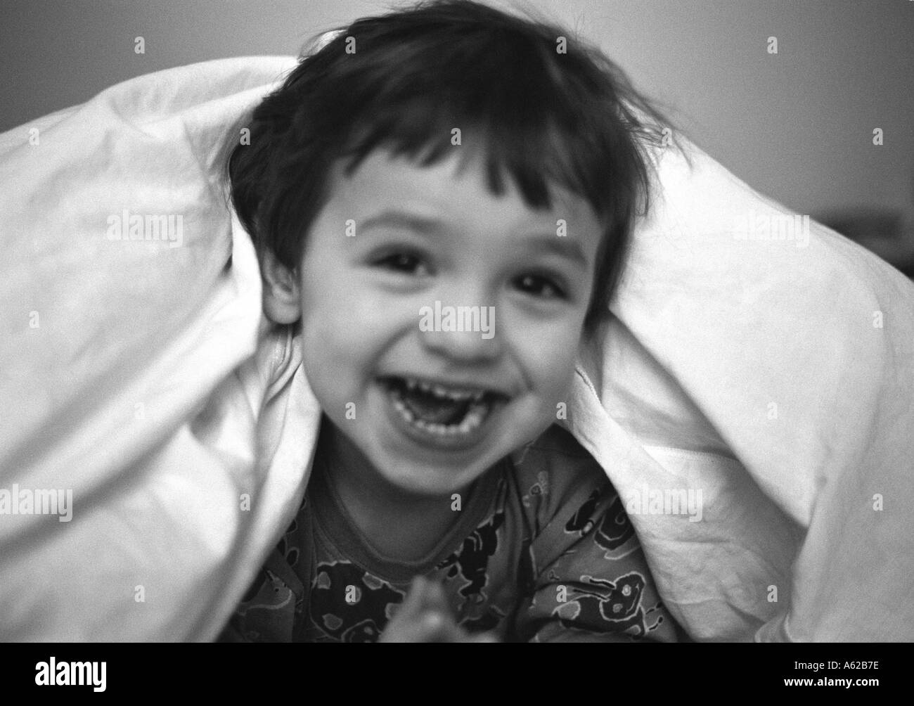 head and shoulders crop of young boy emerging from a duvet laughing