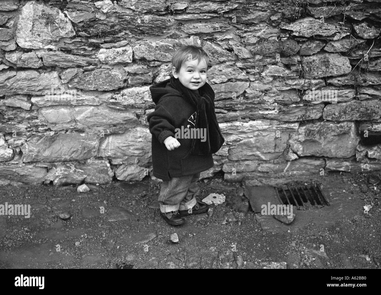 small boy in big jacket stood in front of a large stone wall Stock Photo -  Alamy