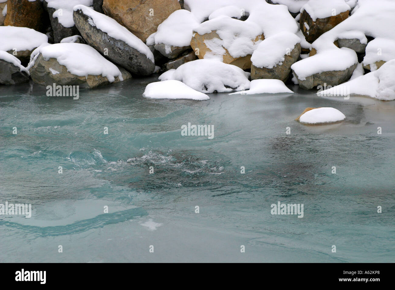 Banff National Park, Alberta, Canada;  Snow covered rocks at water's edge. Stock Photo