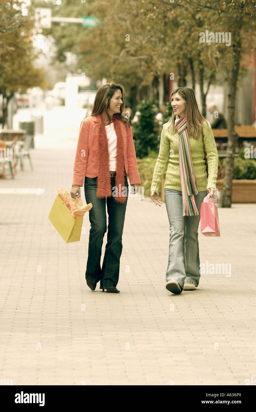 Two young women walking on footpath and carrying shopping bags Stock ...
