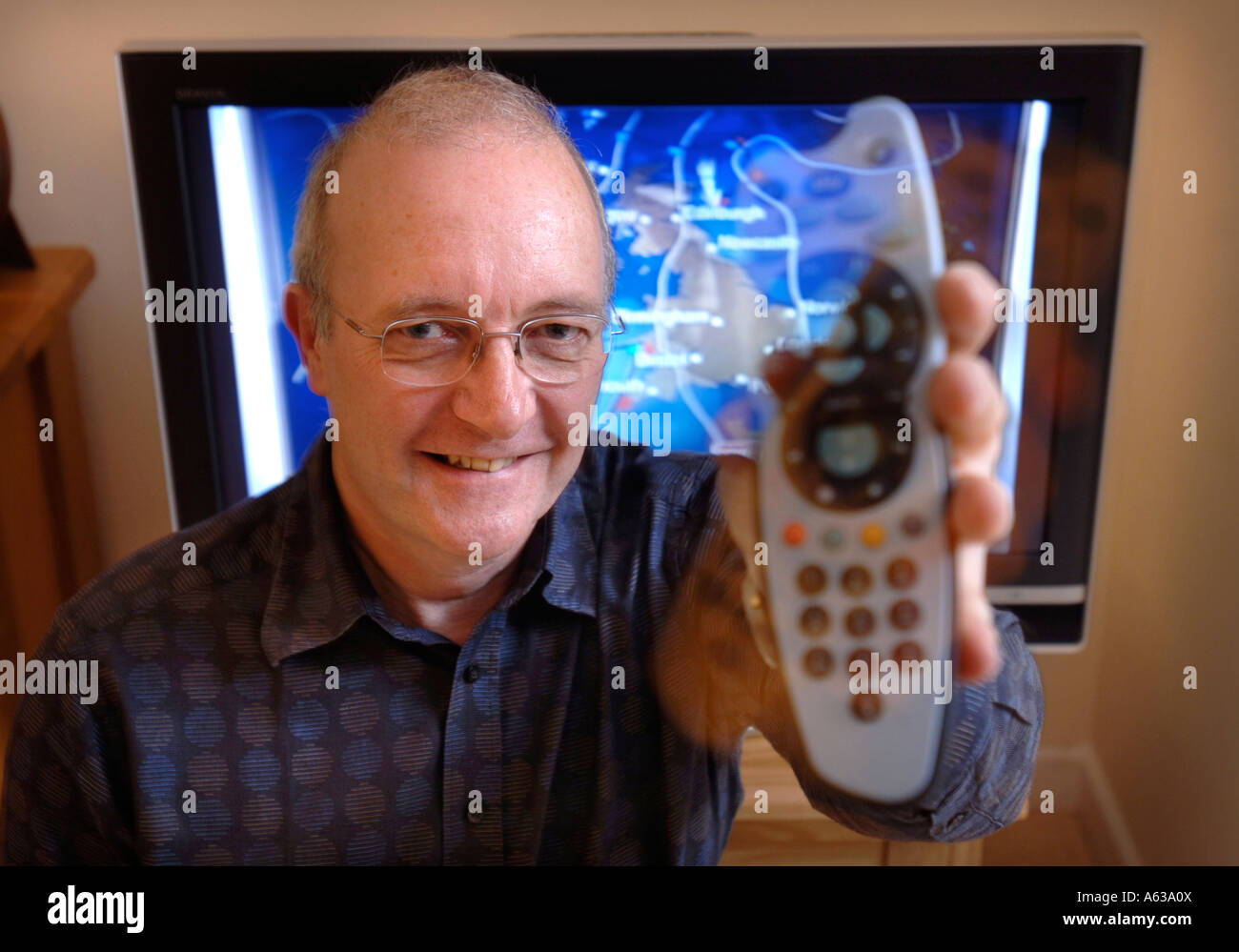 A MIDDLE AGED MAN WITH A REMOTE CONTROL WHILE A WEATHER FORECAST PROGRAMME APPEARS ON TELEVISION UK Stock Photo
