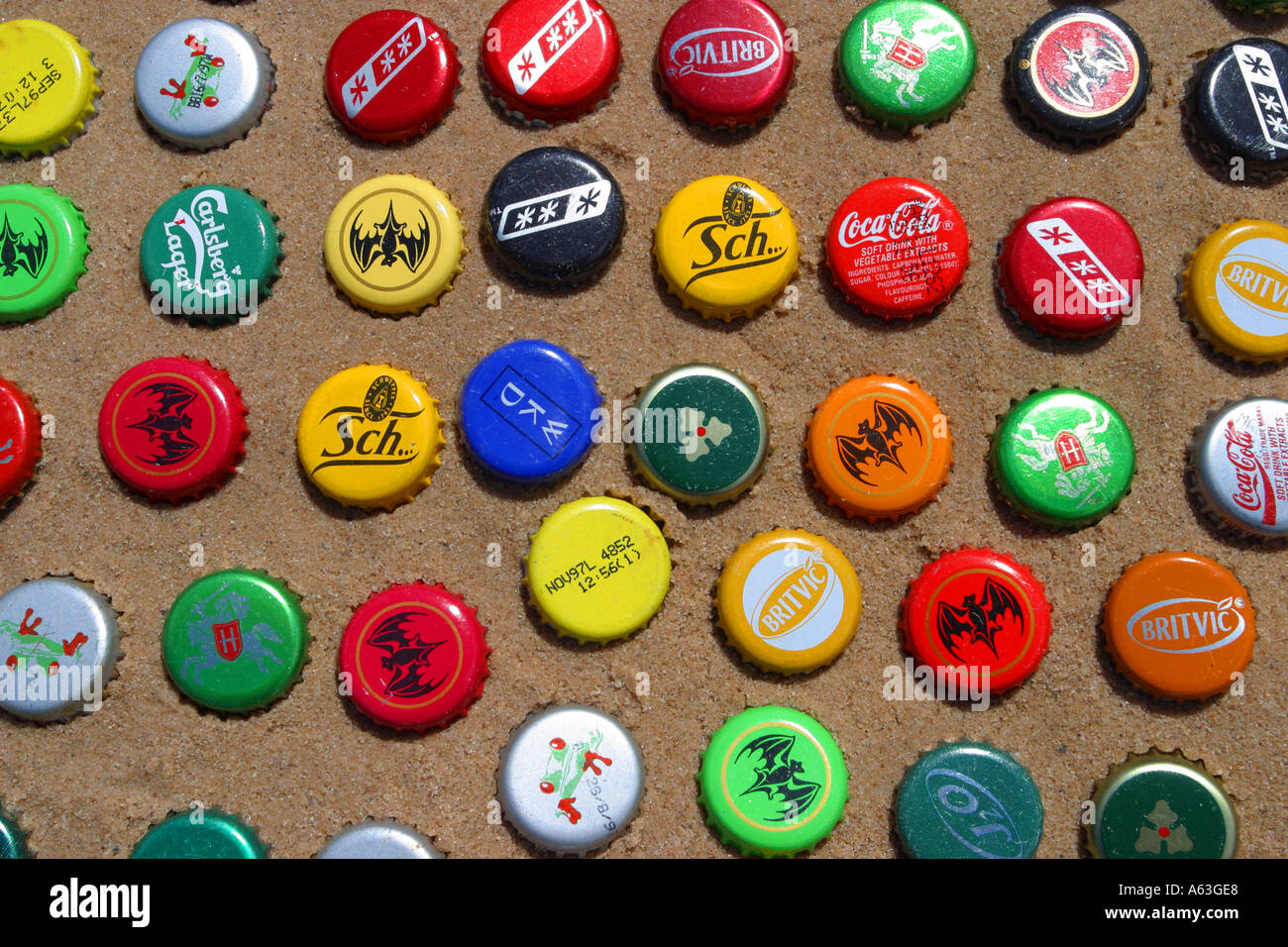 Multi coloured beer bottle tops displayed on sand as beach art Stock