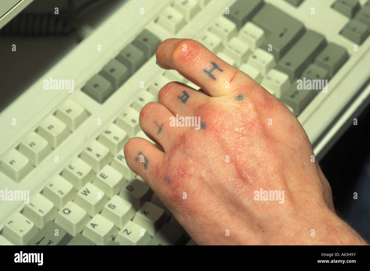 Close up of a hand tattooed with the letters H A T E, with QWERTY keyboard. Lone Wolf? Stock Photo