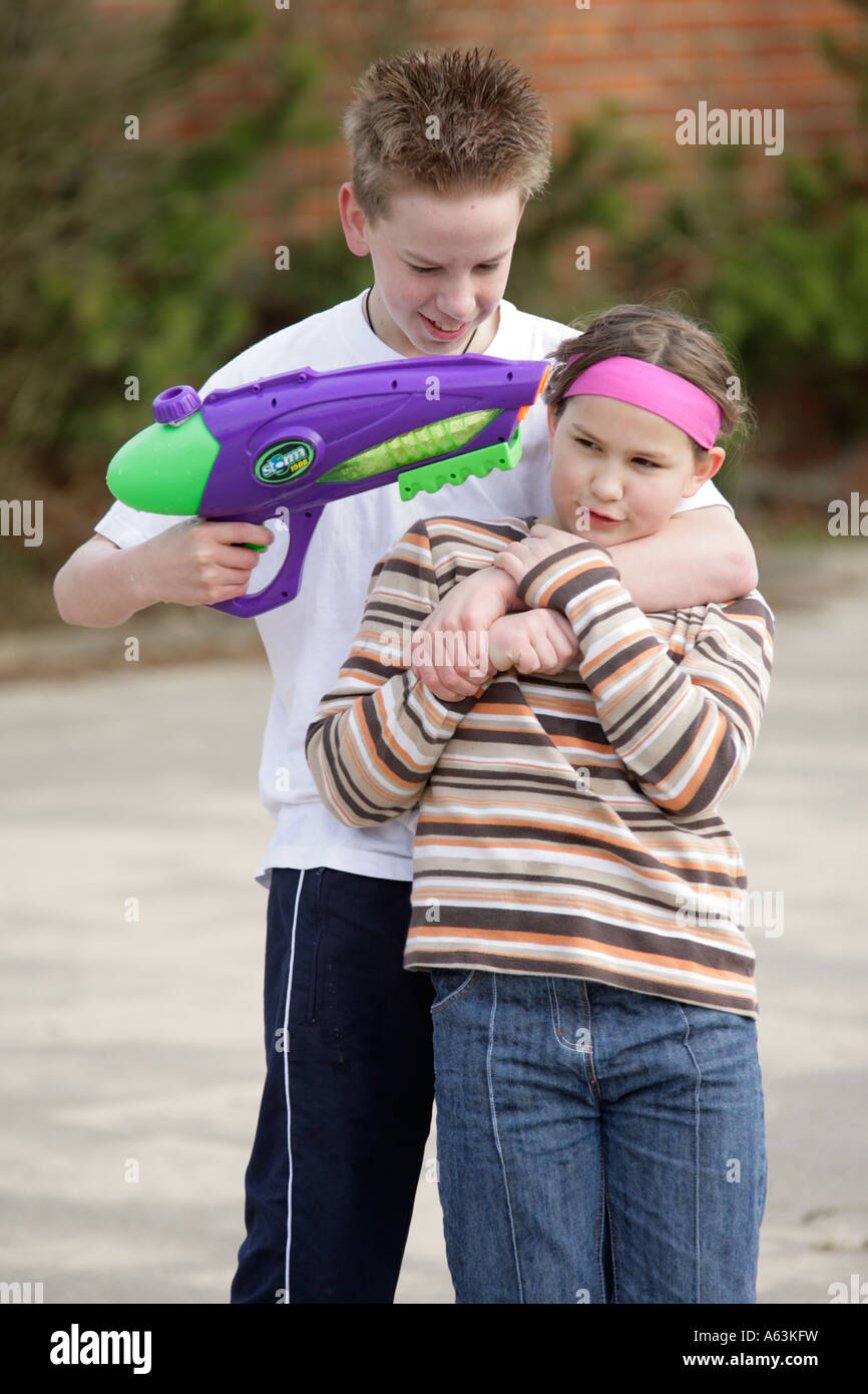 young boy pointing his toy pistol at a little girl´s head in play Stock Photo