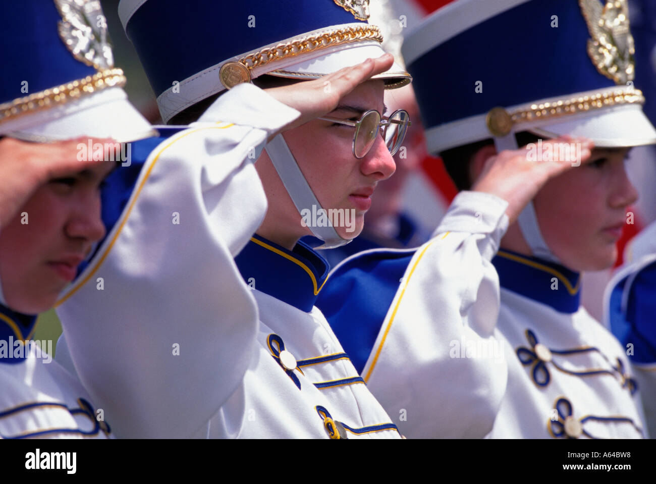 Three marching band members salute American flag as it passes in Parade