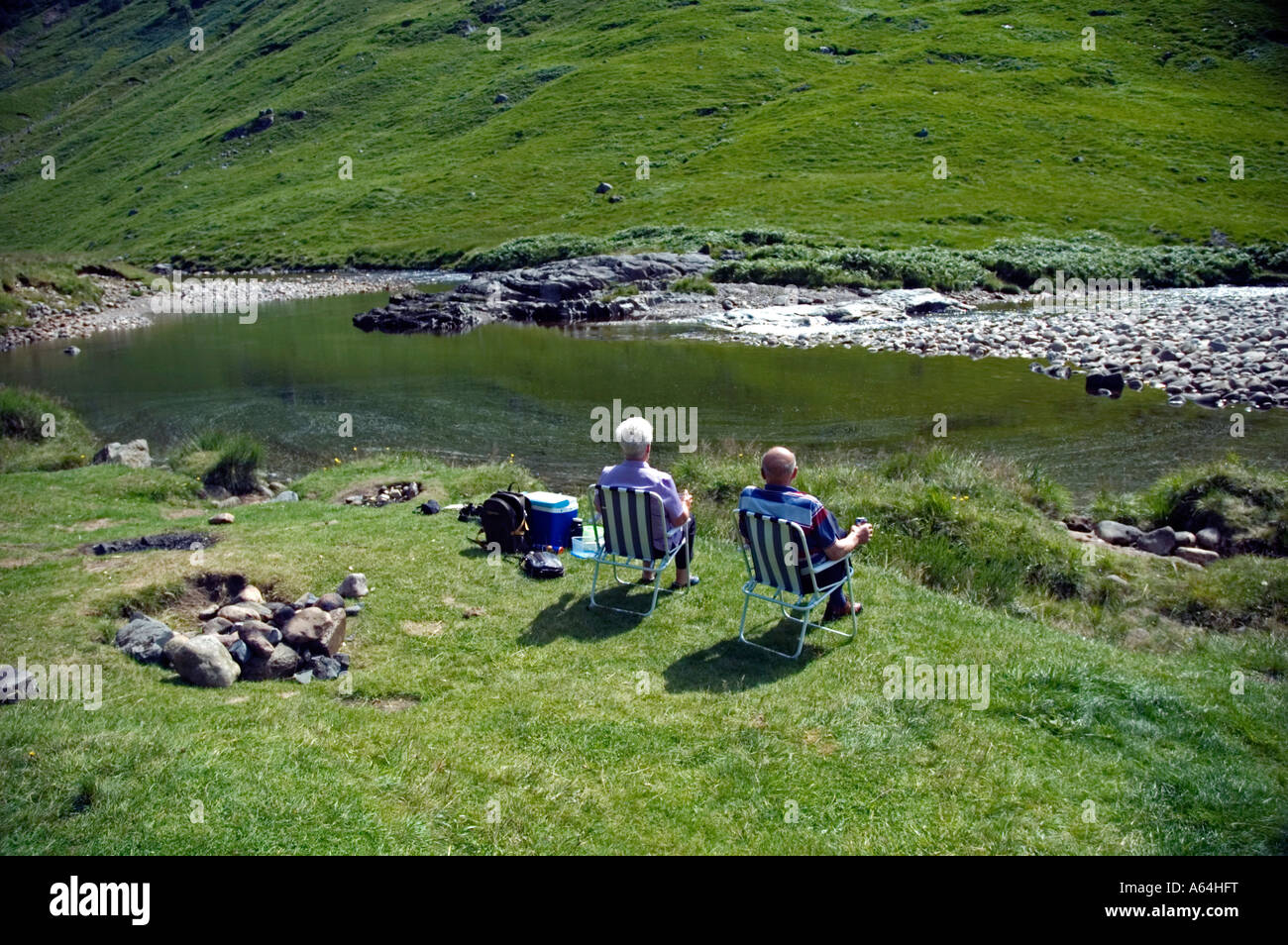 An elderly couple relaxing  in the summer sunshine on a river bank. Stock Photo