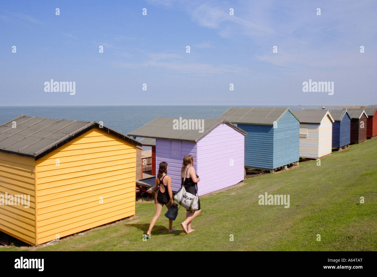 two people walking past beach huts at Tankerton, Kent, UK Stock Photo