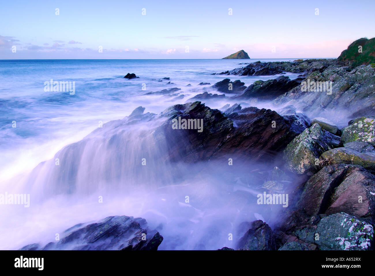 Beautiful dawn light at Wembury Beach with the sea cascading over the exposed rocks and the Mew Stone on the horizon Stock Photo