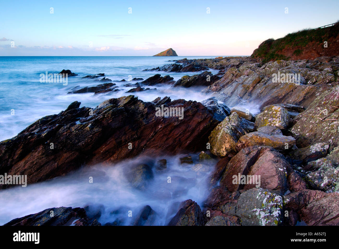 Beautiful dawn light at Wembury Beach with the sea cascading over the exposed rocks and the Mew Stone on the horizon Stock Photo