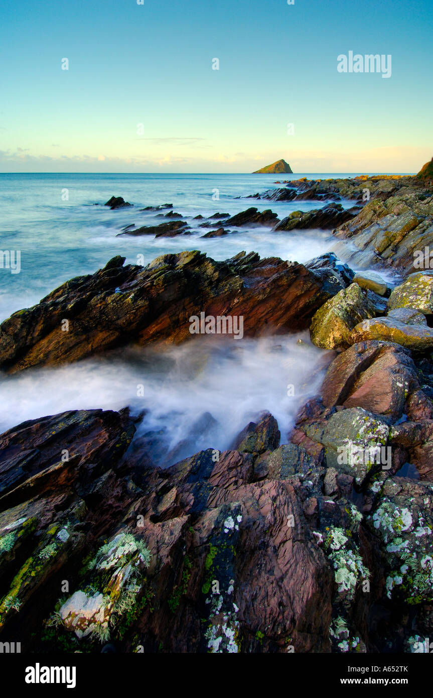 Beautiful dawn light at Wembury Beach with the sea cascading over the exposed rocks and the Mew Stone on the horizon Stock Photo