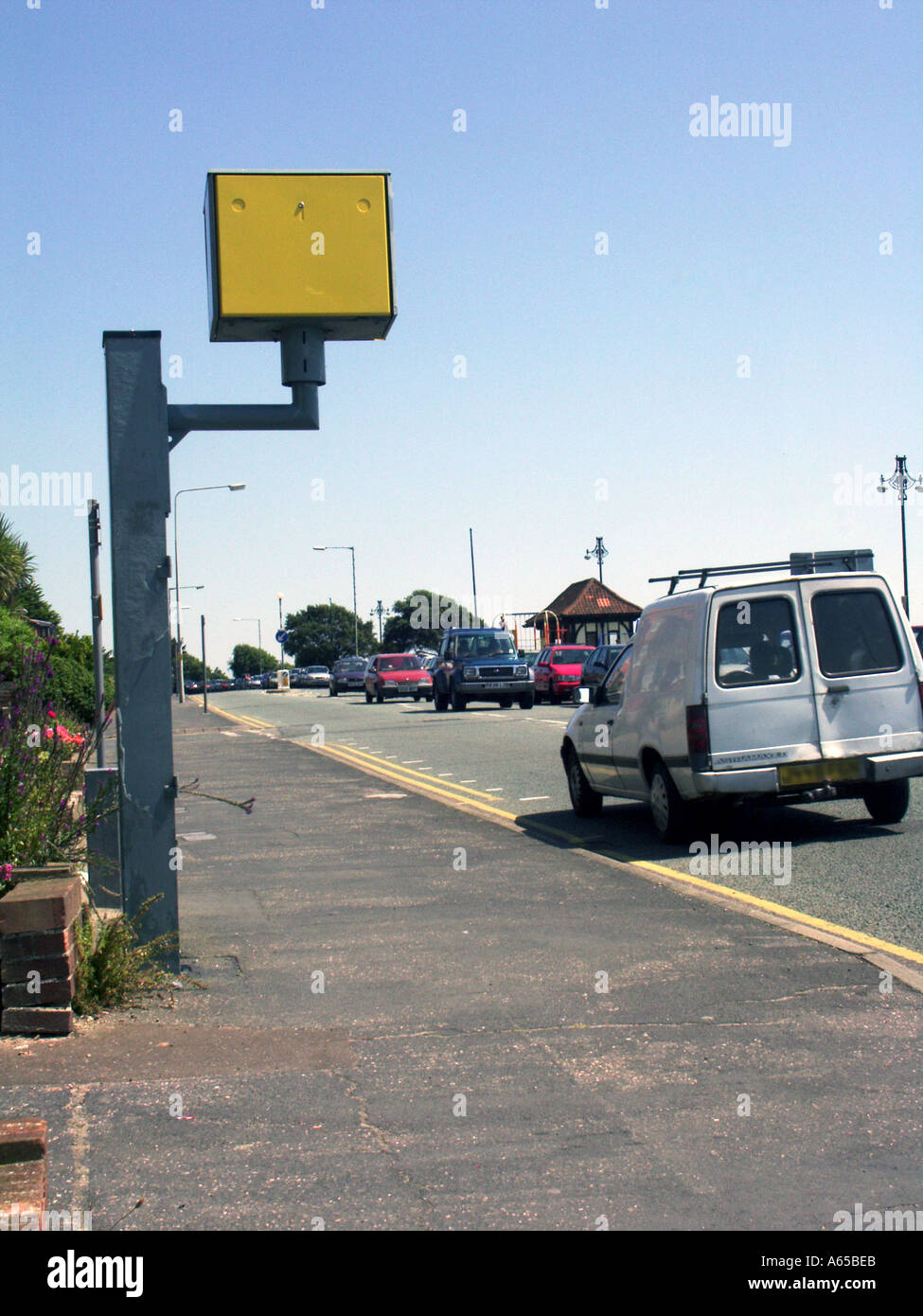 Speed camera on pavement painted conspicuous yellow beside road back view of passing white van obscured number plate Clacton Essex England UK Stock Photo