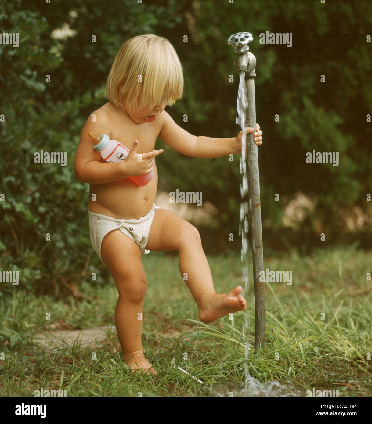 small boy rinsing foot under outdoor faucet Stock Photo
