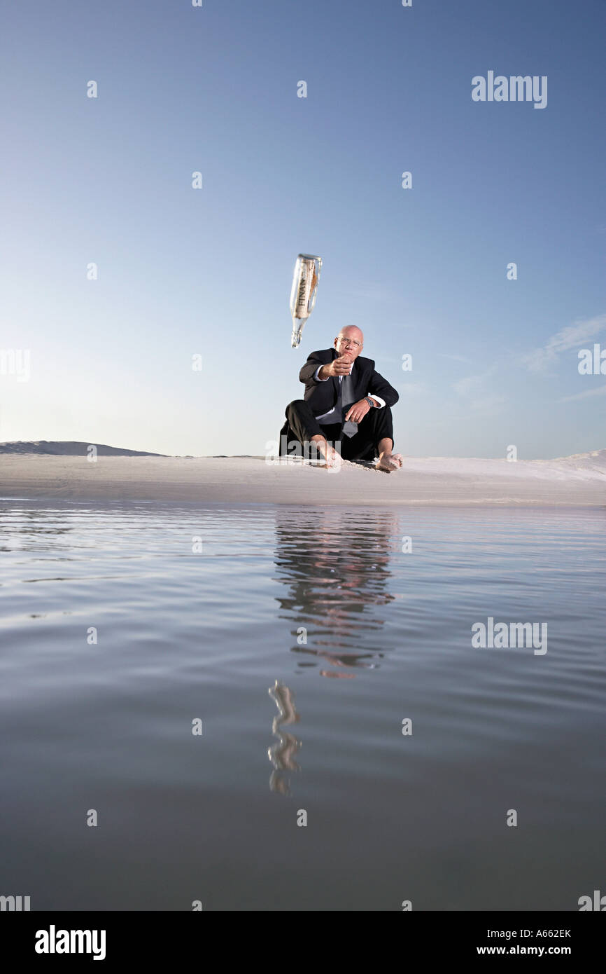 Business man sitting on beach, throwing message in bottle into sea, low angle view Stock Photo