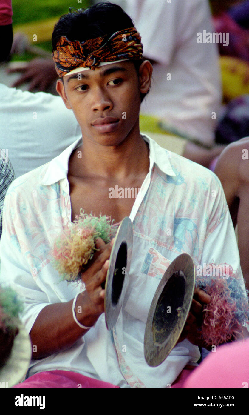 A young man plays small cymbals at a funeral procession in Bali Indonesia Stock Photo