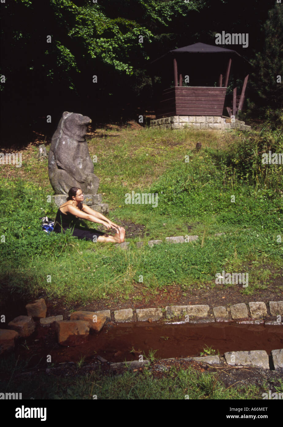Girl Sits Beside Bear Statue and Red Water of Mineral Stream in Woods Marianske Lazne Spa West Bohemia Czech Republic 2004 MR Stock Photo