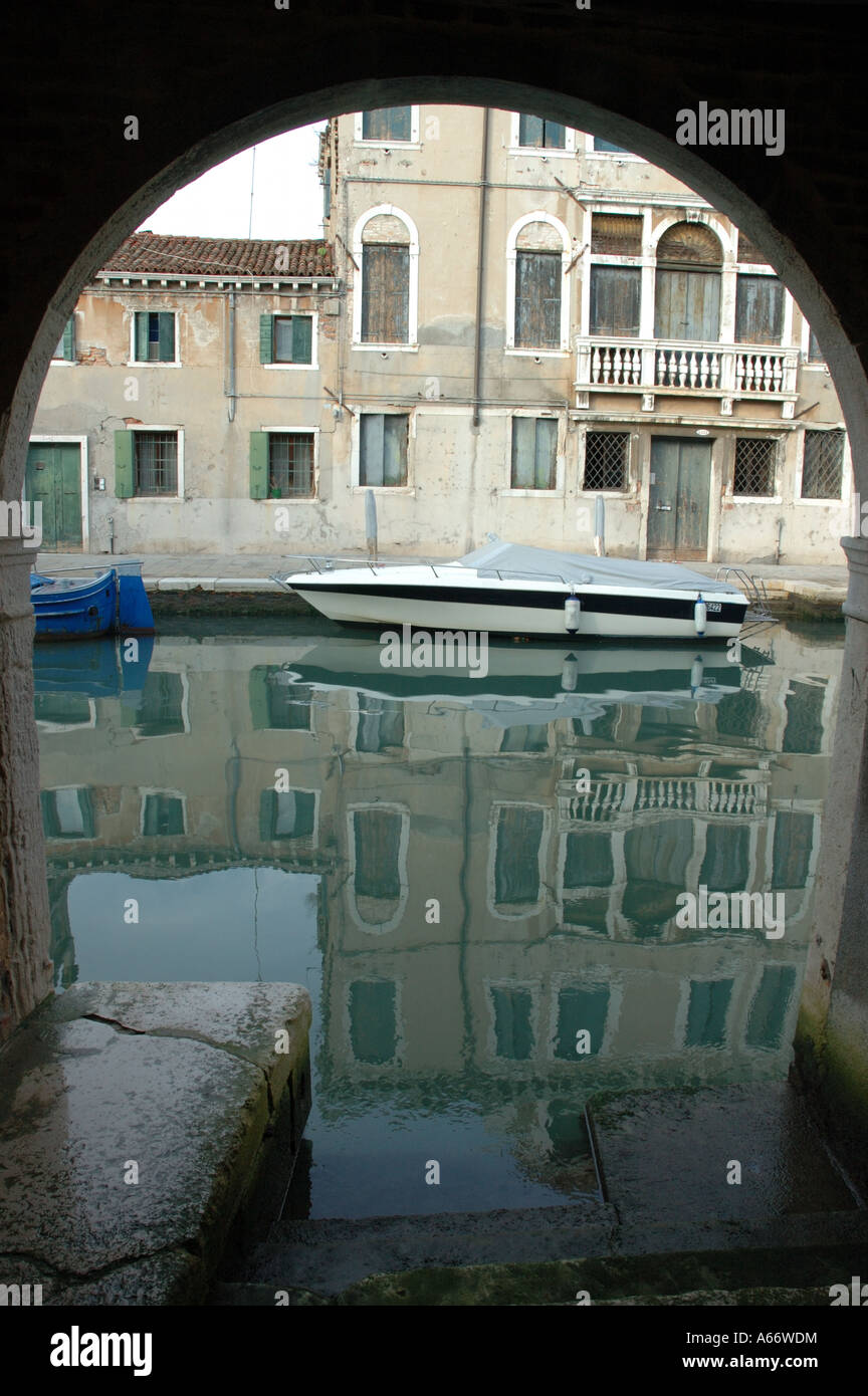 A Venetian canal through an arch with the reflection of a house on the ...