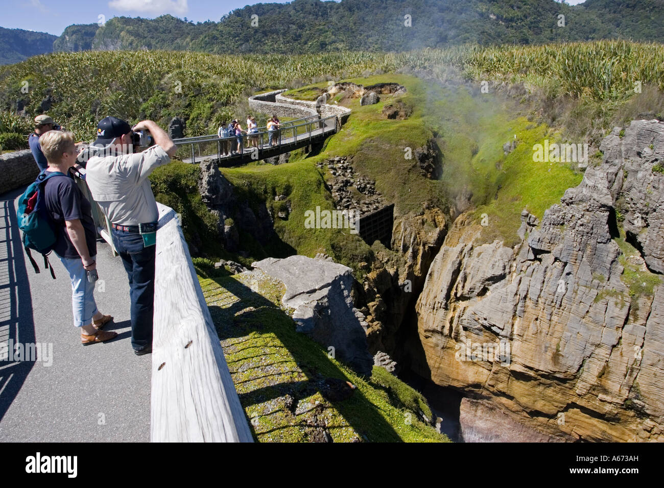 Visitors photographing blowholes in limestone outcrops on cliffs at Pancake Rocks Punakaiki South Island New Zealand Stock Photo