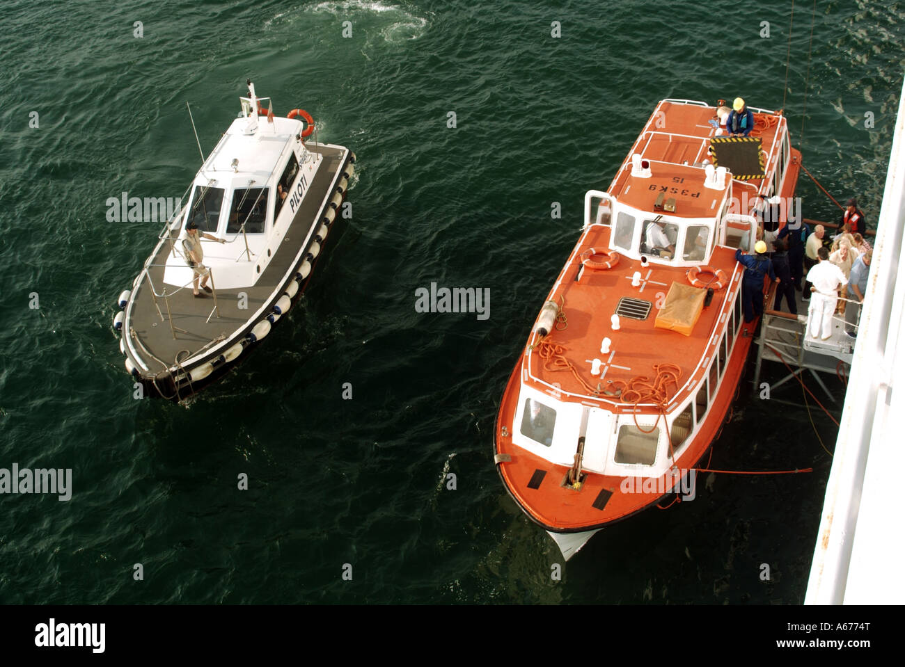 Crew supervise unloading passengers off tender lifeboat onto cruise ship Pilot launch waits to deliver Pilot Stock Photo