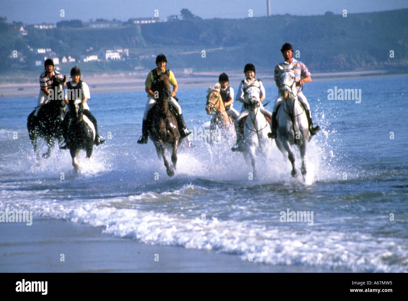 Horse riders gallop through surf on beach ride at St Ouen's Bay, Jersey, Channel  Islands Stock Photo - Alamy