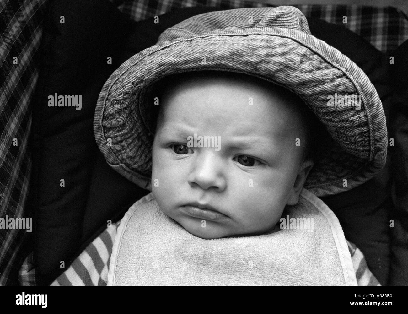 head and shoulder crop of small baby wearing a bib and a large hat pushed back Stock Photo Alamy