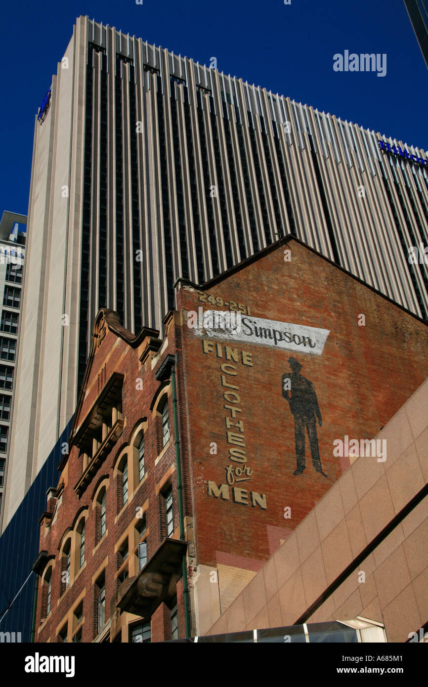 An advertisement for a tailor of a bygone era adorns an older building amongst the behemoths of the modern age Stock Photo