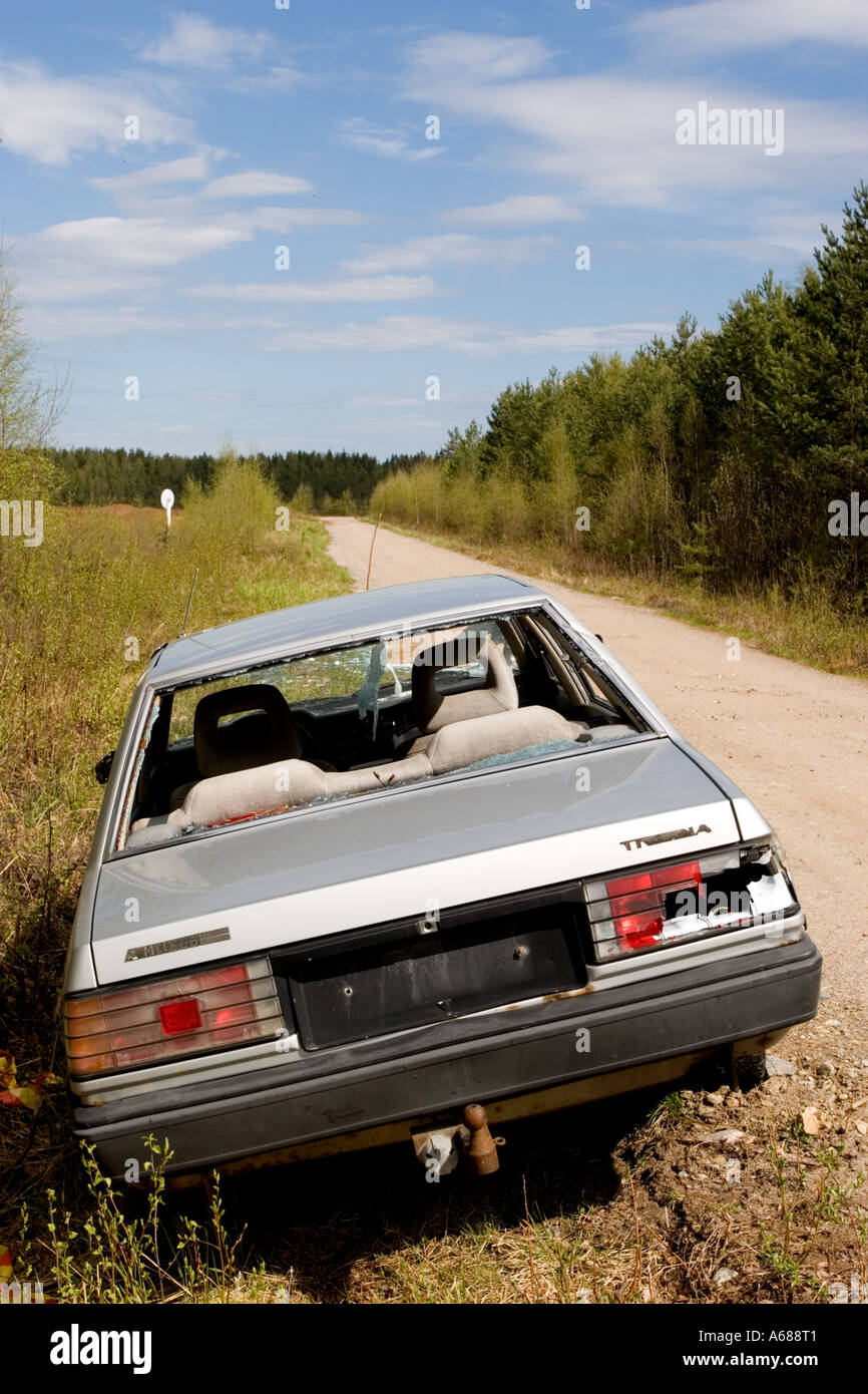 Silver colored abandoned and vandalized sedan at roadside on a side-road , Finland Stock Photo
