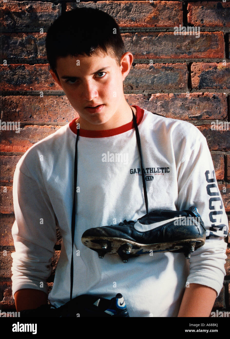 Young Boy footballer with football boot around his neck against a brick wall. Stock Photo