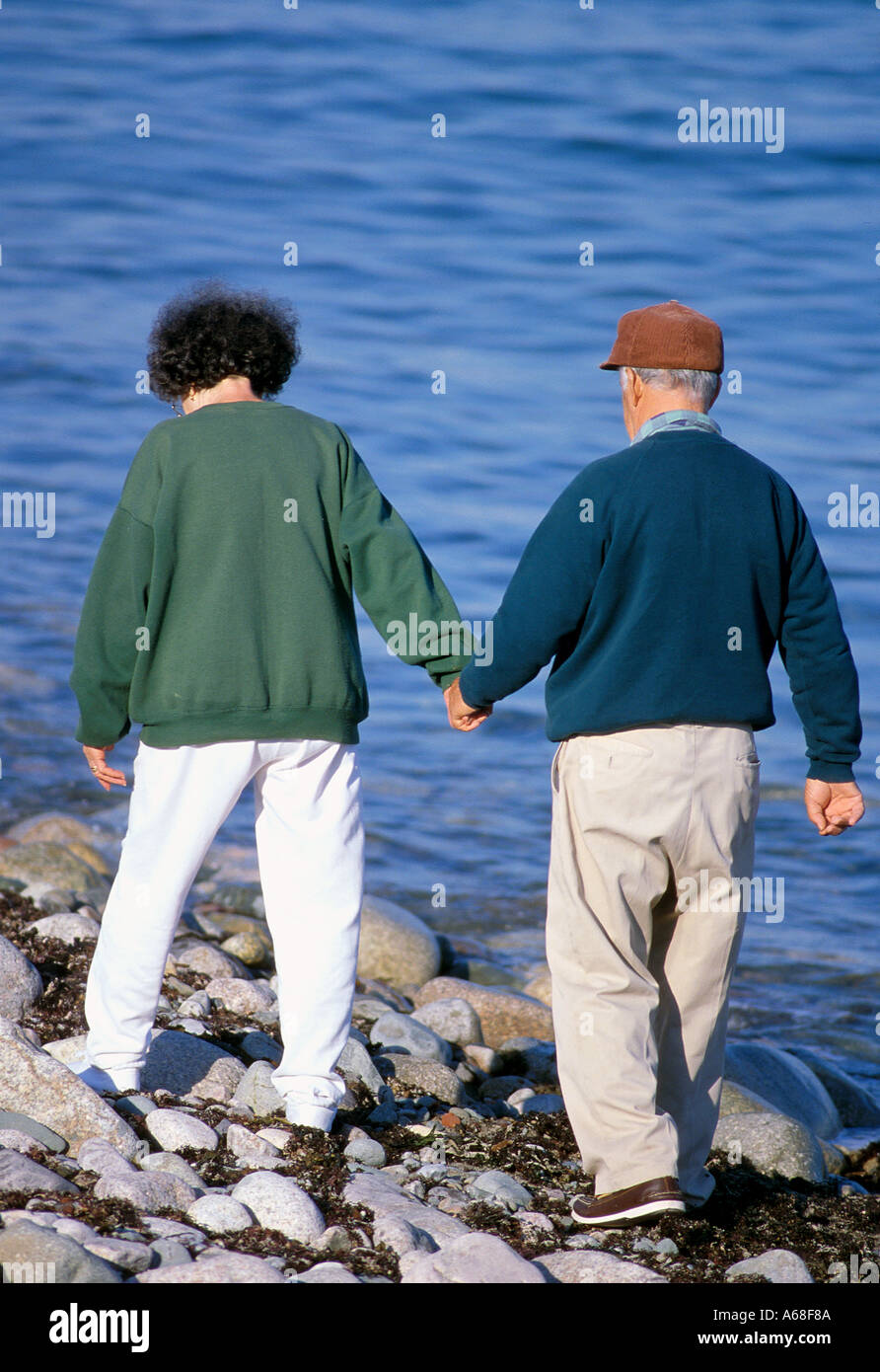 A senior couple hold hands as they walk on the shore Stock Photo