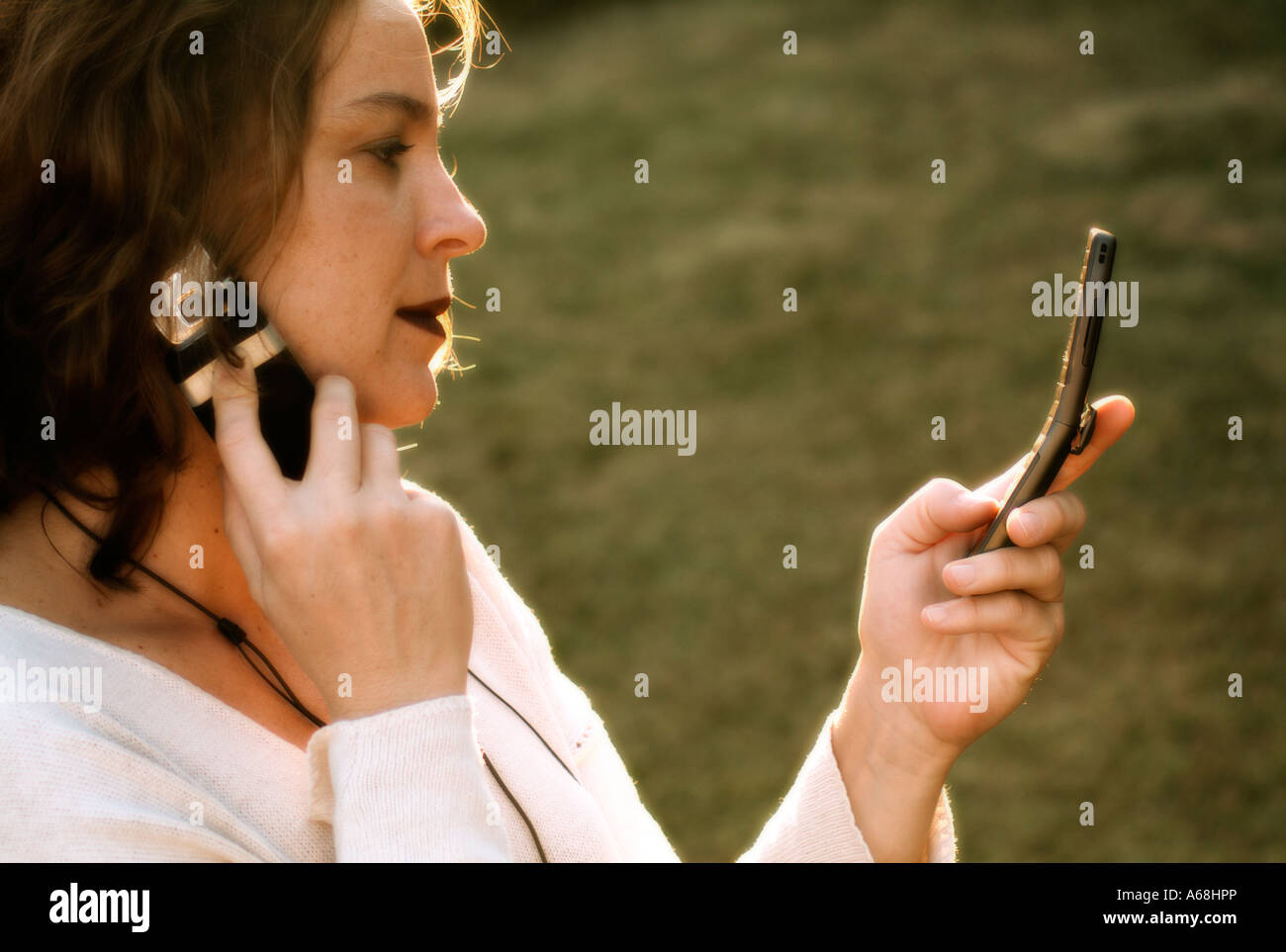 Young girl talking by one cellular phone while read the screen of another one Stock Photo