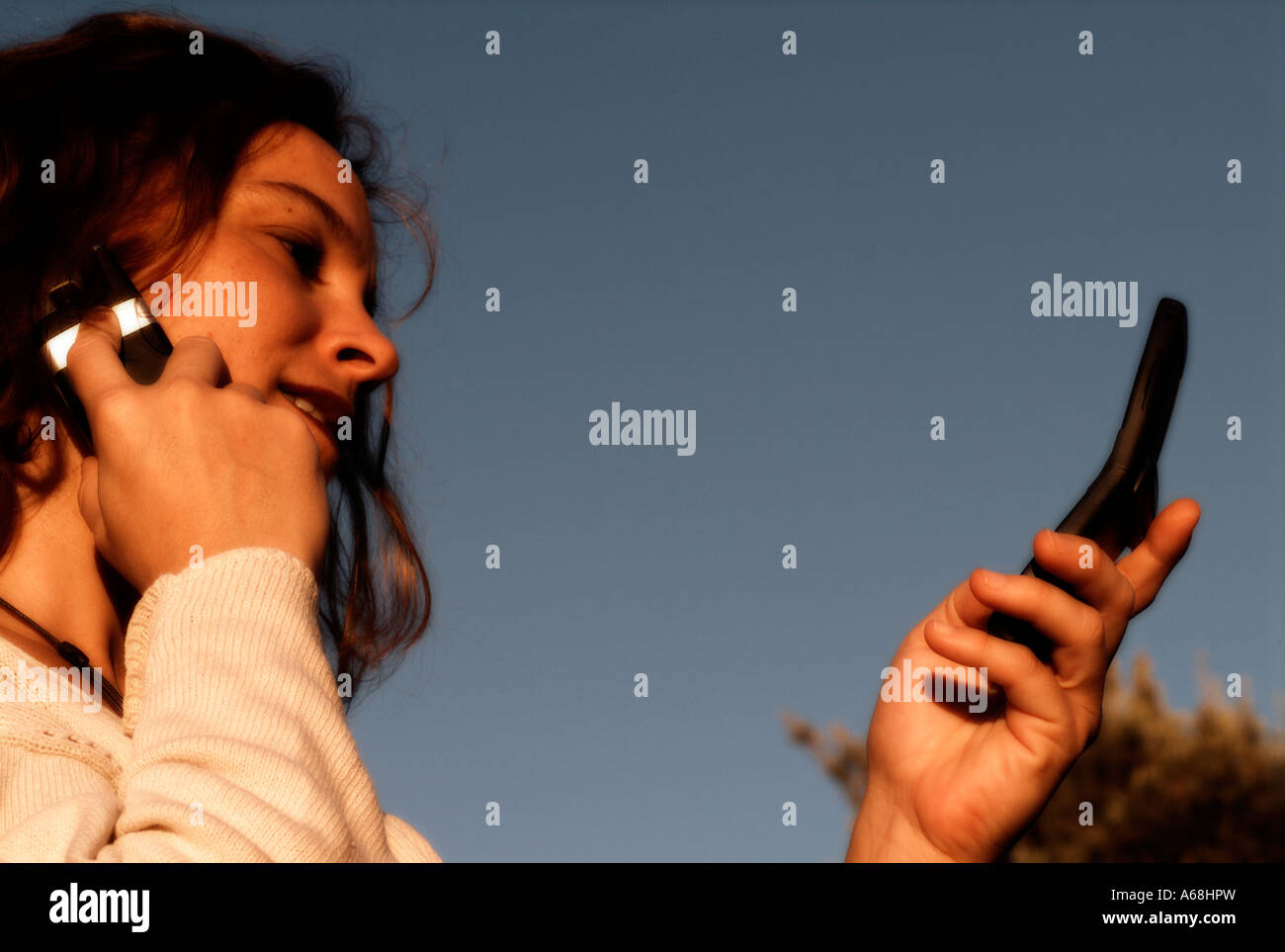 Young girl talking by one cellular phone while read the screen of another one Stock Photo
