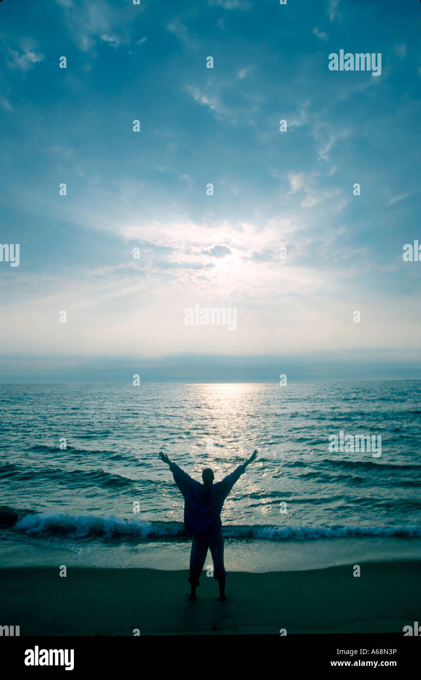 Woman stretches while watching the sunrise over the ocean Stock Photo