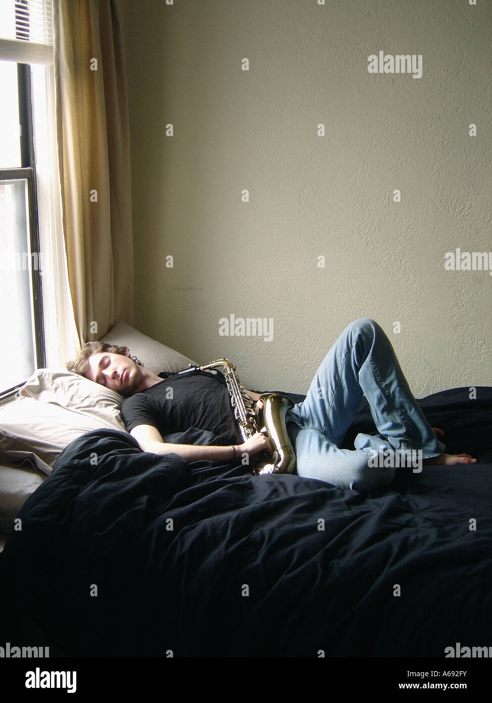 Portrait of Sleeping Man Lying in Bed With a Saxophone He is Wearing Blue Jeans And A Black Tee Shirt t shirt Stock Photo