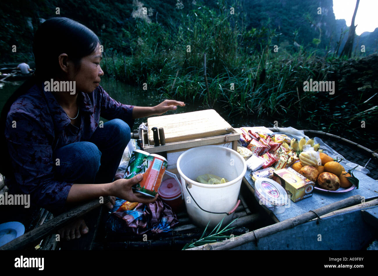 Woman in rowboat selling snacks and softdrinks to tourists, Ngo Dong River, Tam Coc., Vietnam. Stock Photo