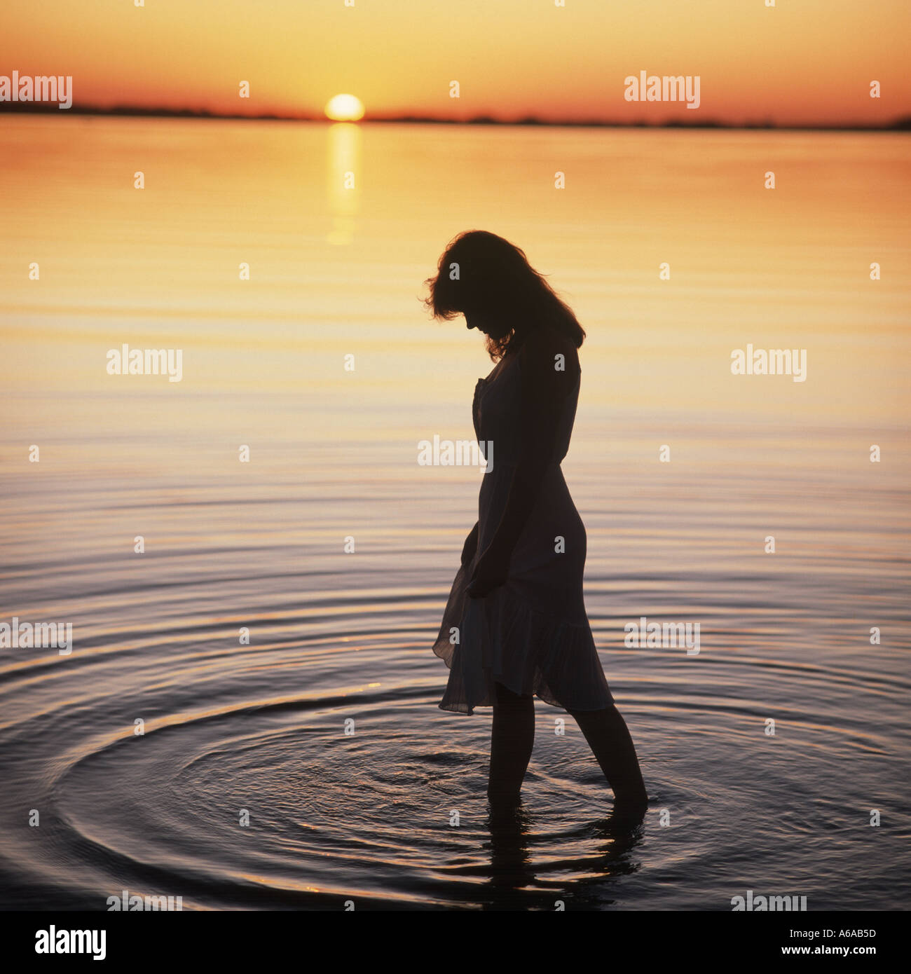 Woman wading in lake at sunset Stock Photo