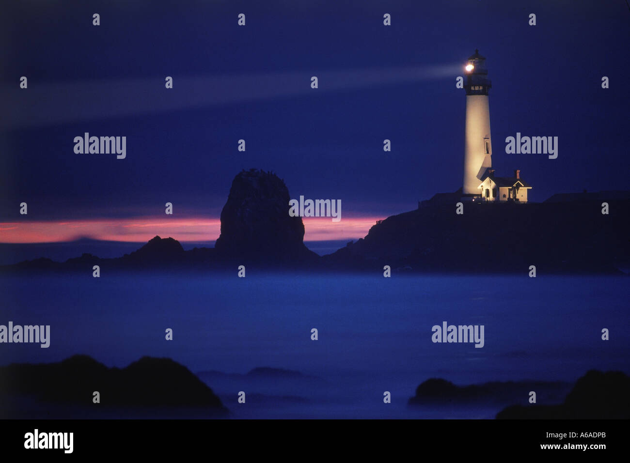 Pigeon Point Lighthouse on rocky ledge over Pacific Ocean in California at dusk Stock Photo