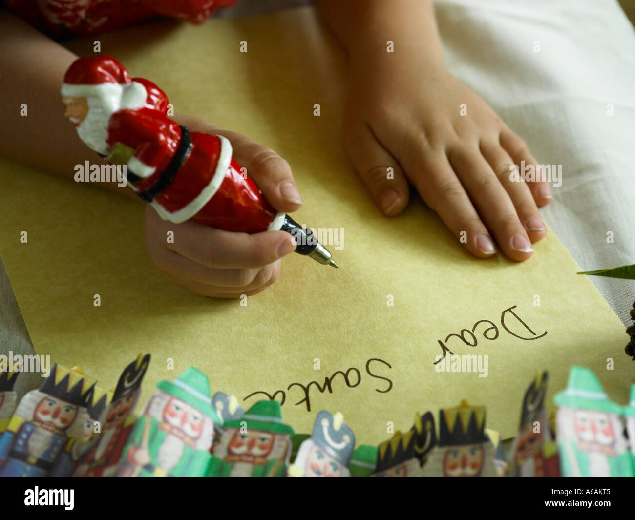 boys hands leaning on table writing dear santa note on paper with father xmas pen with paper christmas decorations Stock Photo