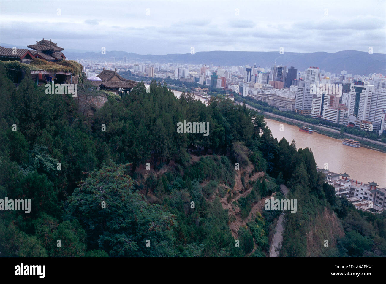 China, Gansu, Lanzhou, Yellow River flanked by lush Baita Shan Gongyuan (White Pagoda Hill Park) and modern city skyline Stock Photo