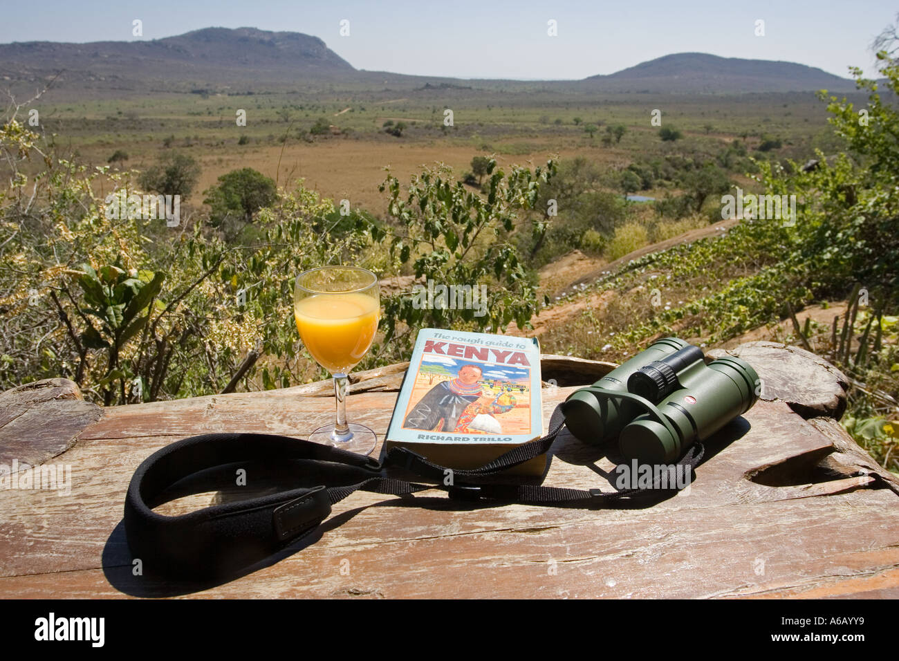 Binoculars Kenya guide book and glass of orange juice on table on veranda at Ngulia Bandas in Tsavo National Park West Kenya Stock Photo