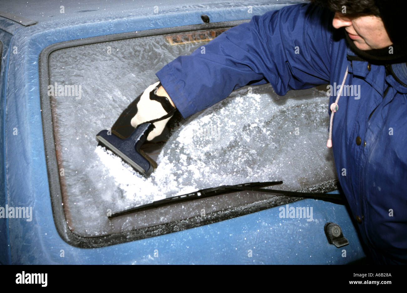 Woman scraping & removing frost from Ford Ka car parked in drive at front of house in warm winter clothing model released Essex England UK Stock Photo
