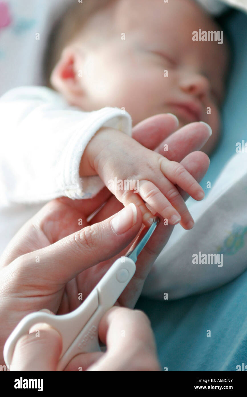 A baby having his fingernails cut using a pair of scissors by his mother Stock Photo