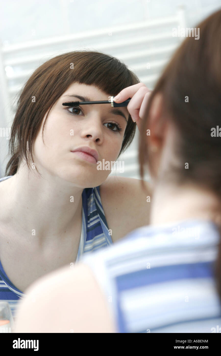 A teenage girl checking her face in a mirror and applying make-up Stock Photo