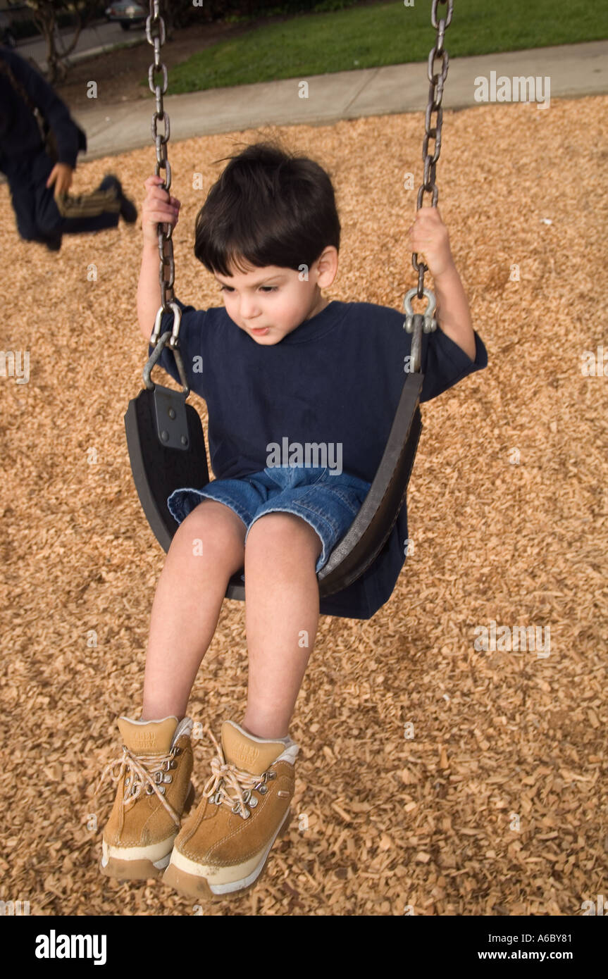 Color vertical image of a toddler wearing a blue Tshirt jean shorts and suede hiking boots swinging on a playground swing Stock Photo