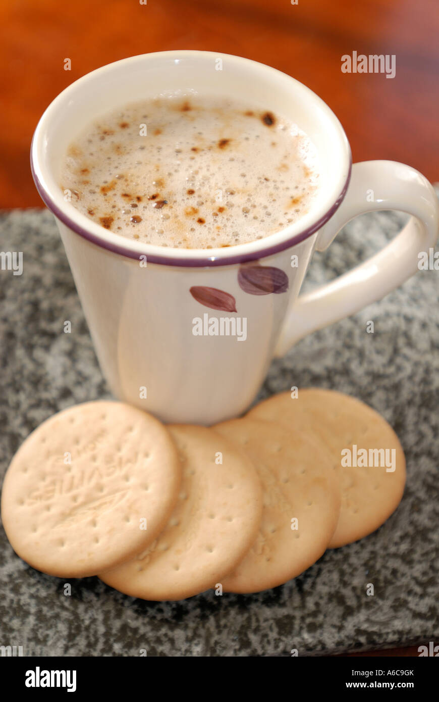 Cup of frothy coffee with four Plain Rich Tea biscuits around the base