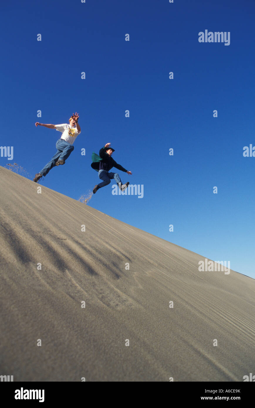 Two young men jumping off sand dune ridge Oregon Dunes National