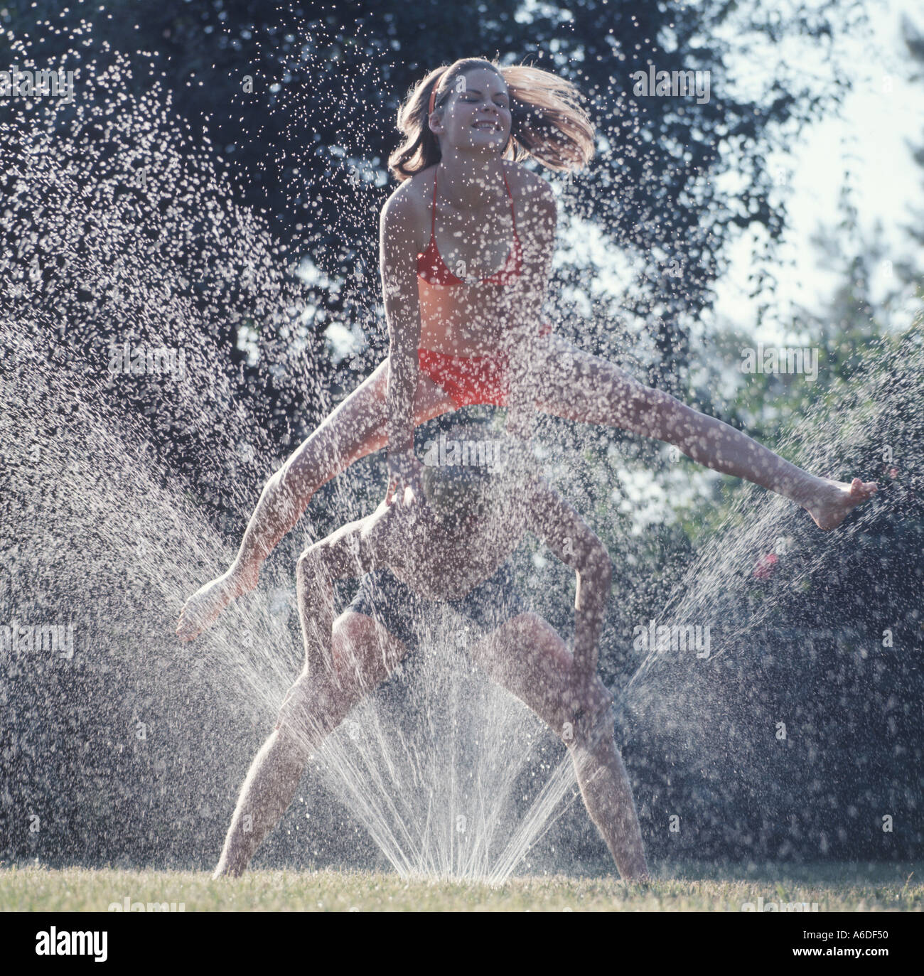 teenagers playing leapfrog in water sprinkler Stock Photo